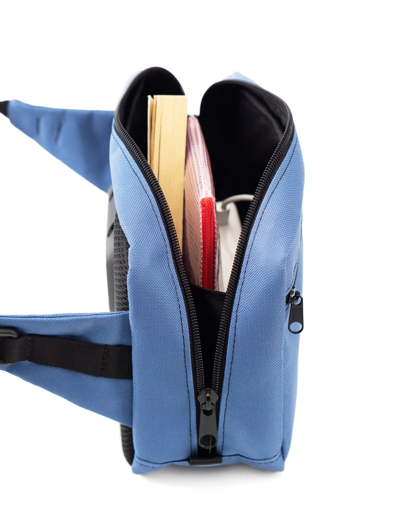 Seitliche Ansicht der hellblauen Crossbody-Bag „Iceblue“ von Spleen Berlin mit sichtbarem Zipper; die Tasche ist geöffnet und zeigt eingelegte Gegenstände. Vegane 3,5-Liter-Umhängetasche im urbanen Stil, auch als Lenkertasche fürs Fahrrad nutzbar. @Spleen Berlin