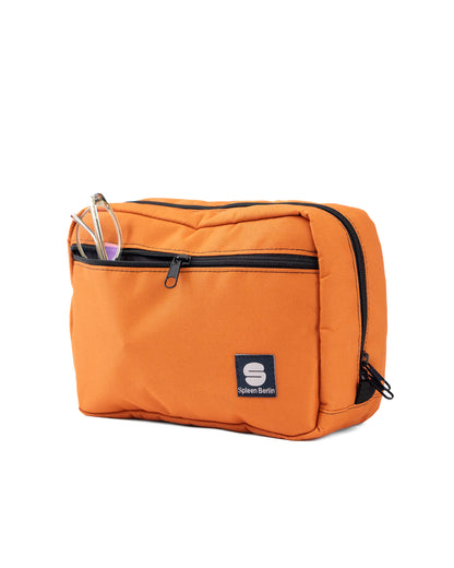 Orangefarbene Crossbody-Bag „Skandinavian Orange“ von Spleen Berlin in Vorderansicht mit sichtbarer Fronttasche und Zipper; in der Fronttasche steckt eine Brille. Vegane 3,5-Liter-Umhängetasche im urbanen Stil, auch als Lenkertasche fürs Fahrrad nutzbar. @Spleen Berlin
